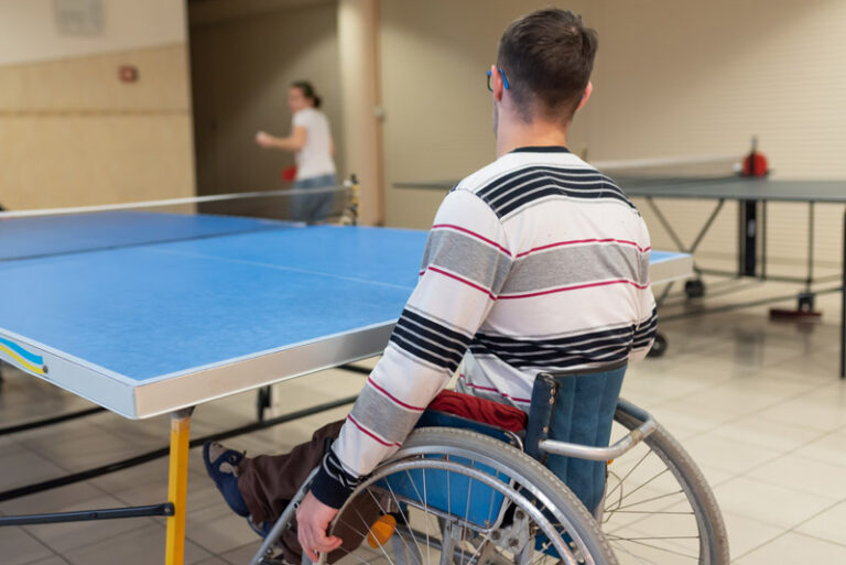 Wheelchair user playing table tennis. From the back.