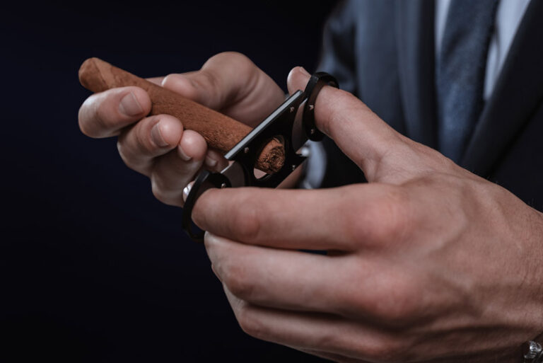 Image of hands holding a guillotine and a cigar. Cigar clubs con